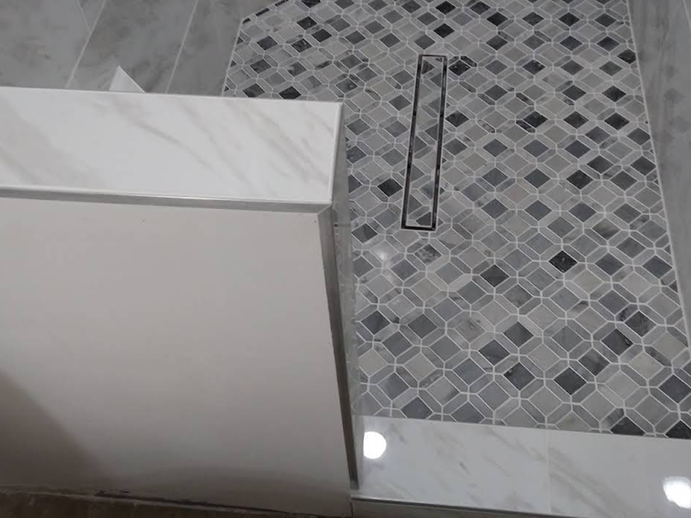 A bathroom with a walk in shower and a drain on the floor.