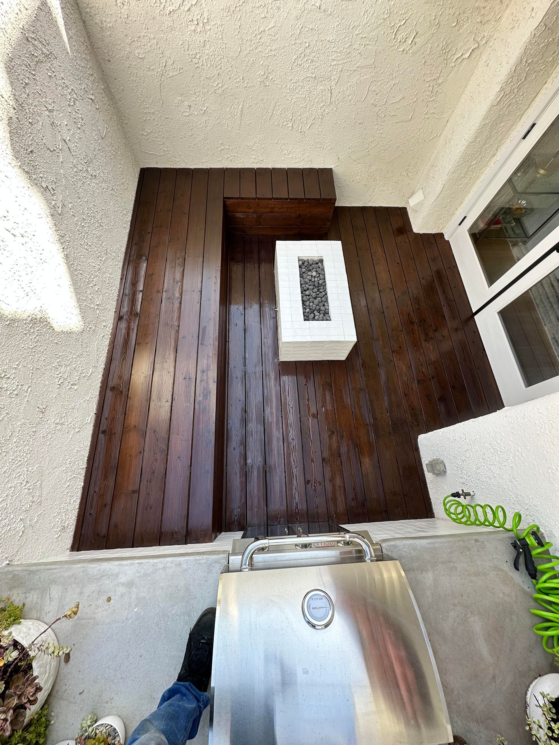 A person is standing on a wooden deck next to a grill.