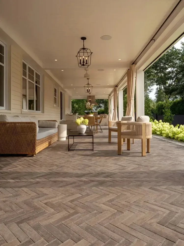 Covered patio with wicker seating, herringbone tile floor, and garden view through open side.