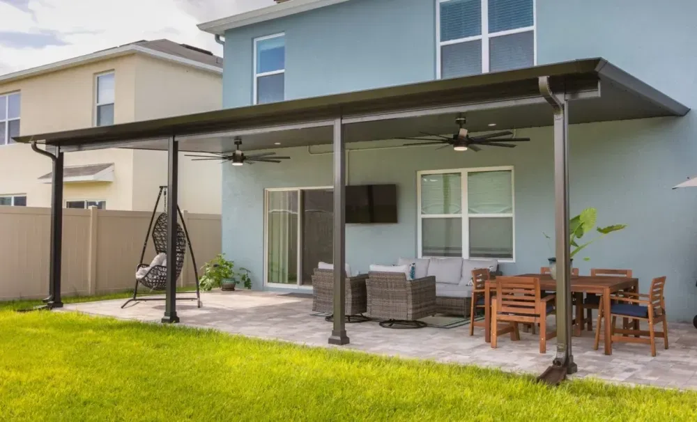 Modern patio with covered seating, dining table, and lawn beside a two-story house