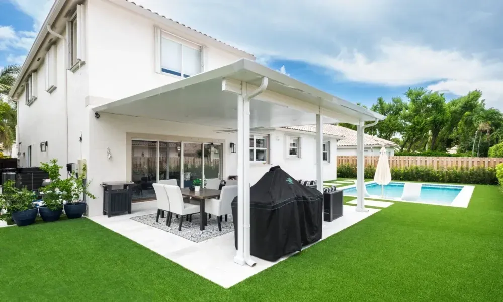 Modern white house patio with outdoor dining, covered grill, and a small pool beside bright green lawn