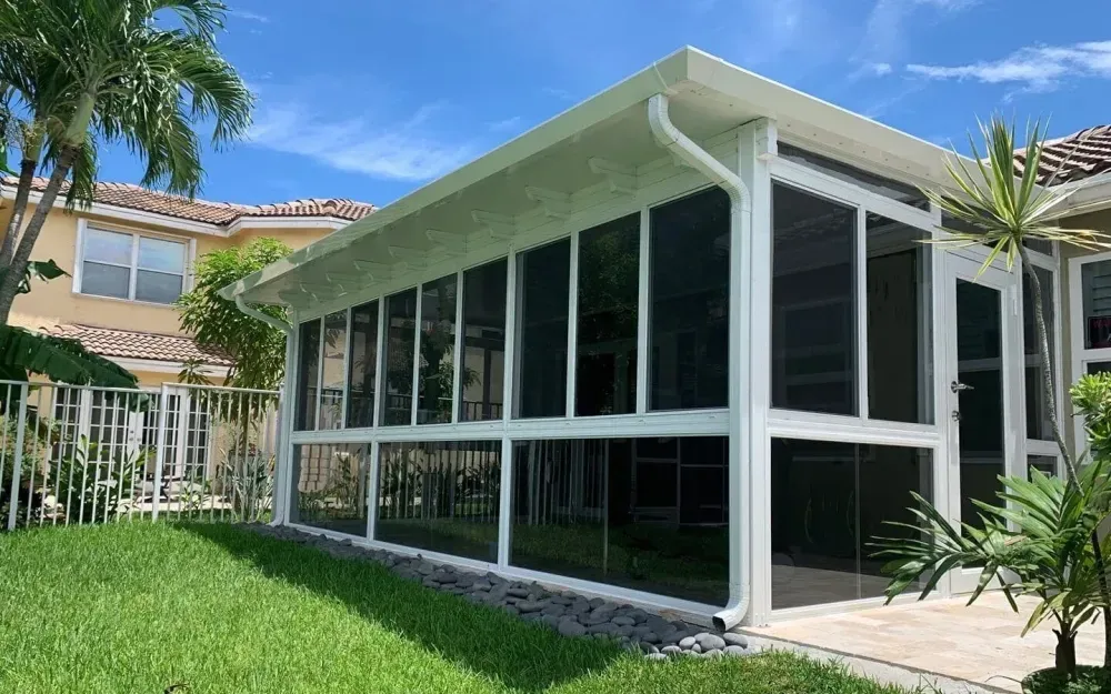 Screened patio enclosure with white frame and glass panels beside a green lawn and house