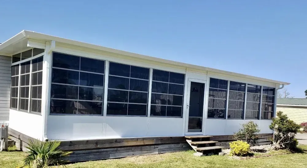 Small white house with large screened windows and a front porch in a sunny yard