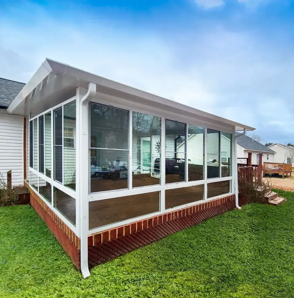 Enclosed porch with white trim and glass windows attached to a house, beside a green lawn.