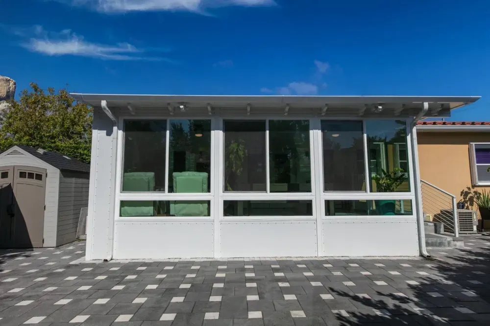 Modern white pavilion with large glass windows and a patterned stone courtyard under a blue sky