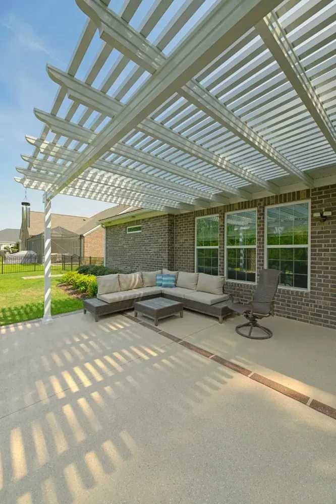 Covered patio with outdoor sectional sofa, glass-top table, and pergola casting striped shadows.