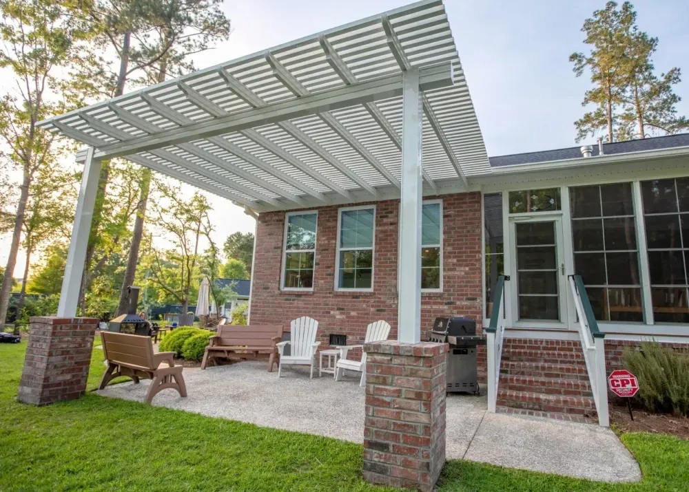 Brick house patio with white pergola, outdoor chairs, and green lawn