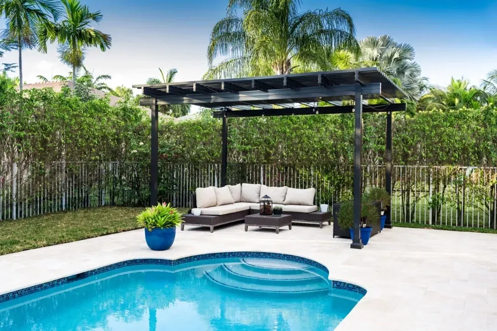 Backyard pool with a shaded lounge cabana, white patio, and lush tropical greenery