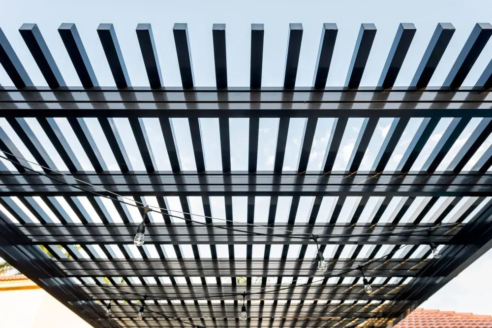 Black metal slatted pergola viewed from below against a blue sky