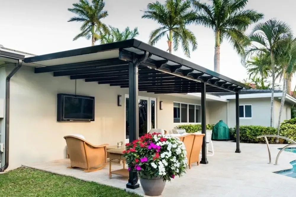 Modern patio beside a white house with wicker chairs, potted flowers, and palm trees in the background