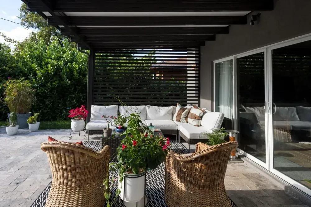 Covered patio with wicker chairs, white sofa, potted flowers, and sliding glass doors