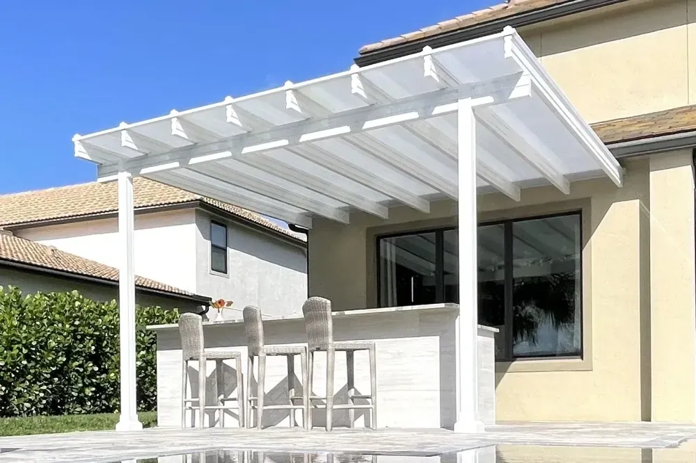 White pergola-covered patio with outdoor dining set beside a beige house and large window