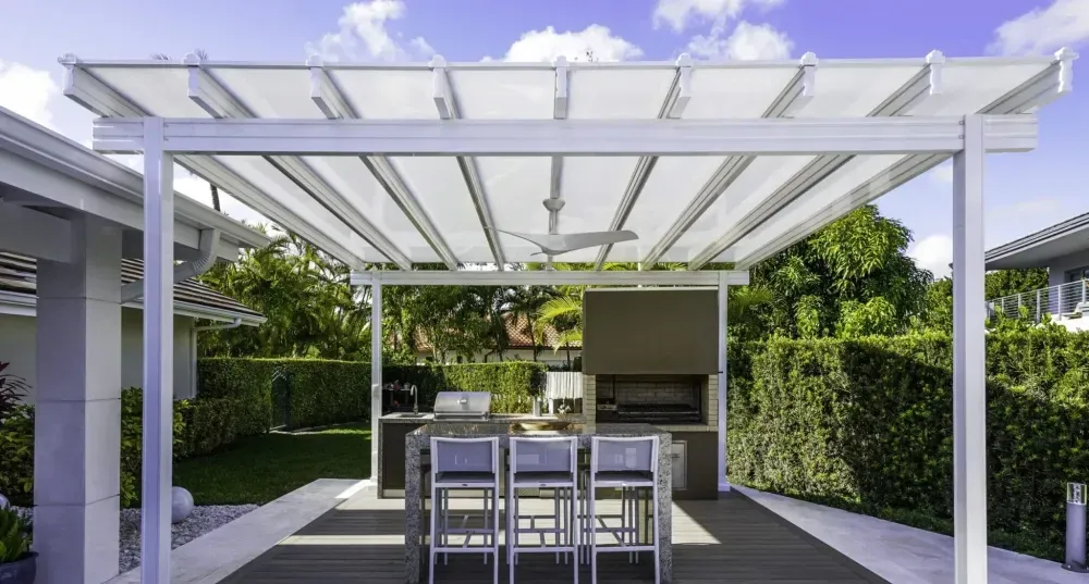 Modern outdoor patio with white pergola, dining table, and hedge-lined backyard kitchen.