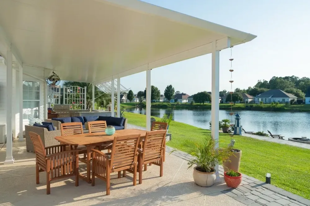 Outdoor patio with wooden dining set overlooking a calm waterfront lawn and houses beyond