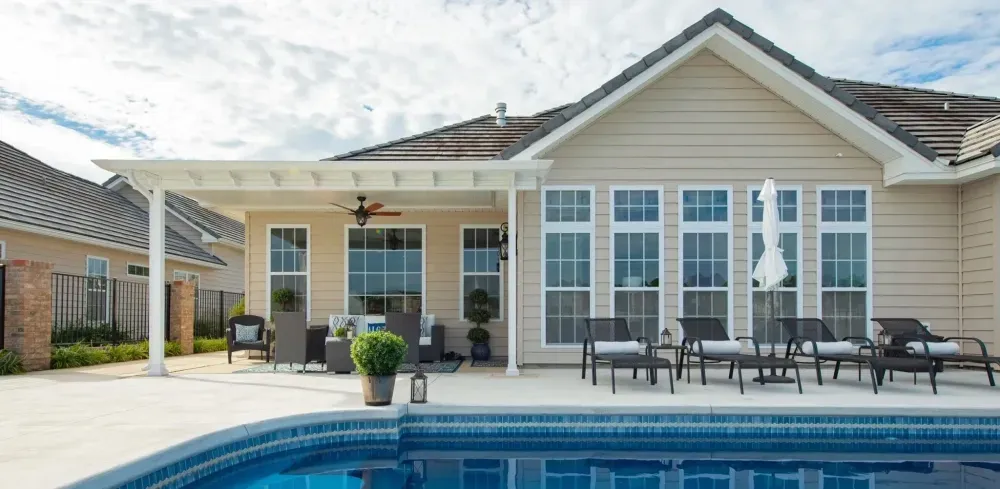 Backyard patio with a swimming pool, lounge chairs, and a beige house with large windows