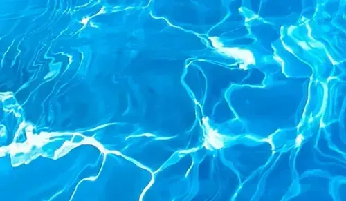 Bright blue swimming pool water with sunlit ripples and reflections