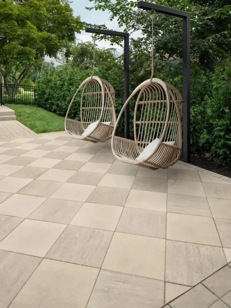 Two hanging wicker egg chairs on a tiled patio beside lush greenery