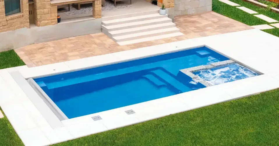 Modern backyard with rectangular blue swimming pool, patio lounge chairs, and green lawn under a bright sky