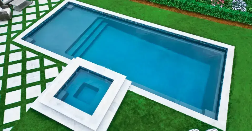 Modern infinity pool beside white patio with lounge chairs, overlooking a blue lake and mountains