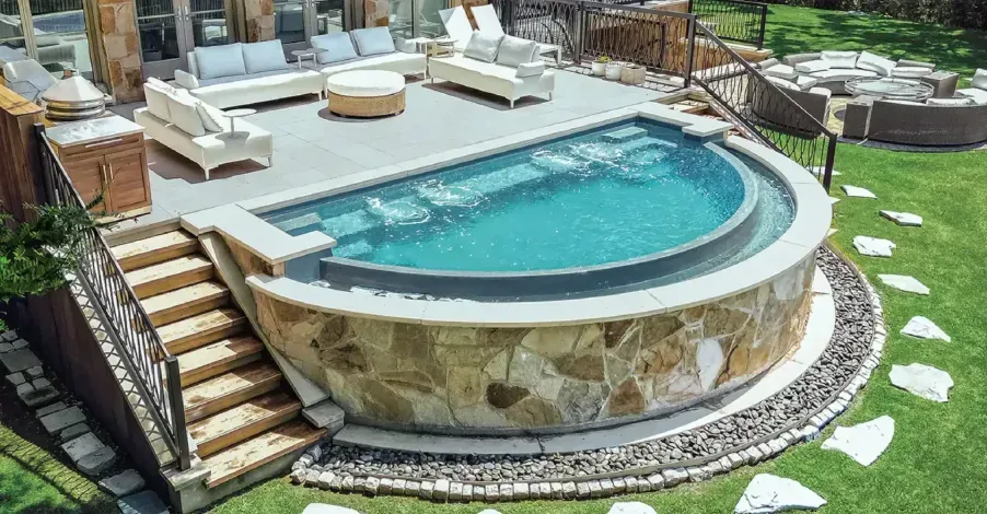 Luxurious backyard pool with curved stone edge, patio seating, and green lawn around it
