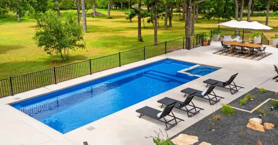Modern pool courtyard with blue water, wood deck, white lounge chairs, and a sleek white house.
