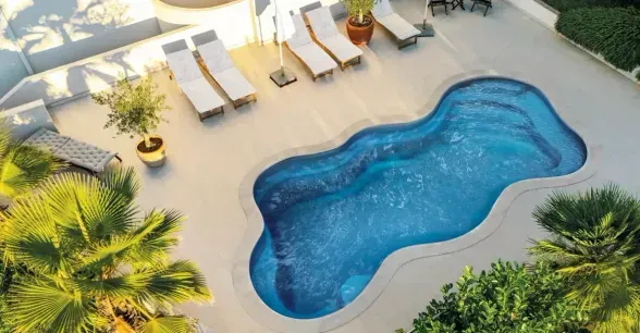 Luxurious backyard pool with curved stone edge, patio seating, and green lawn around it