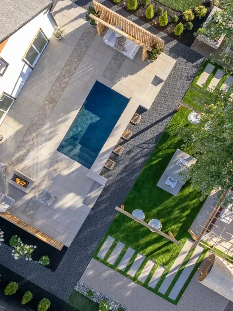 Aerial view of a modern backyard with a rectangular pool, patio seating, and green lawn.