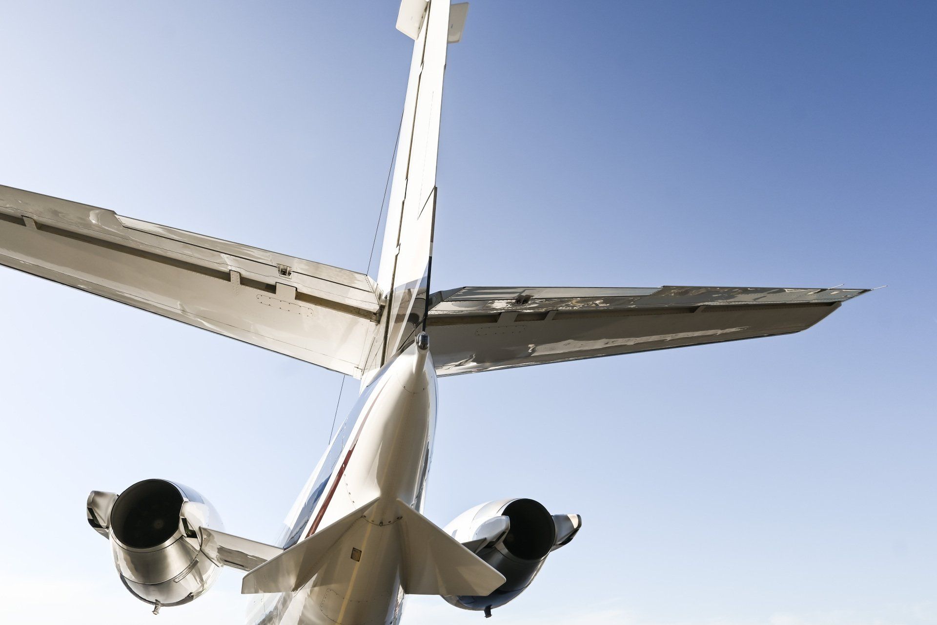 Underside view of a white airplane in flight against a clear blue sky