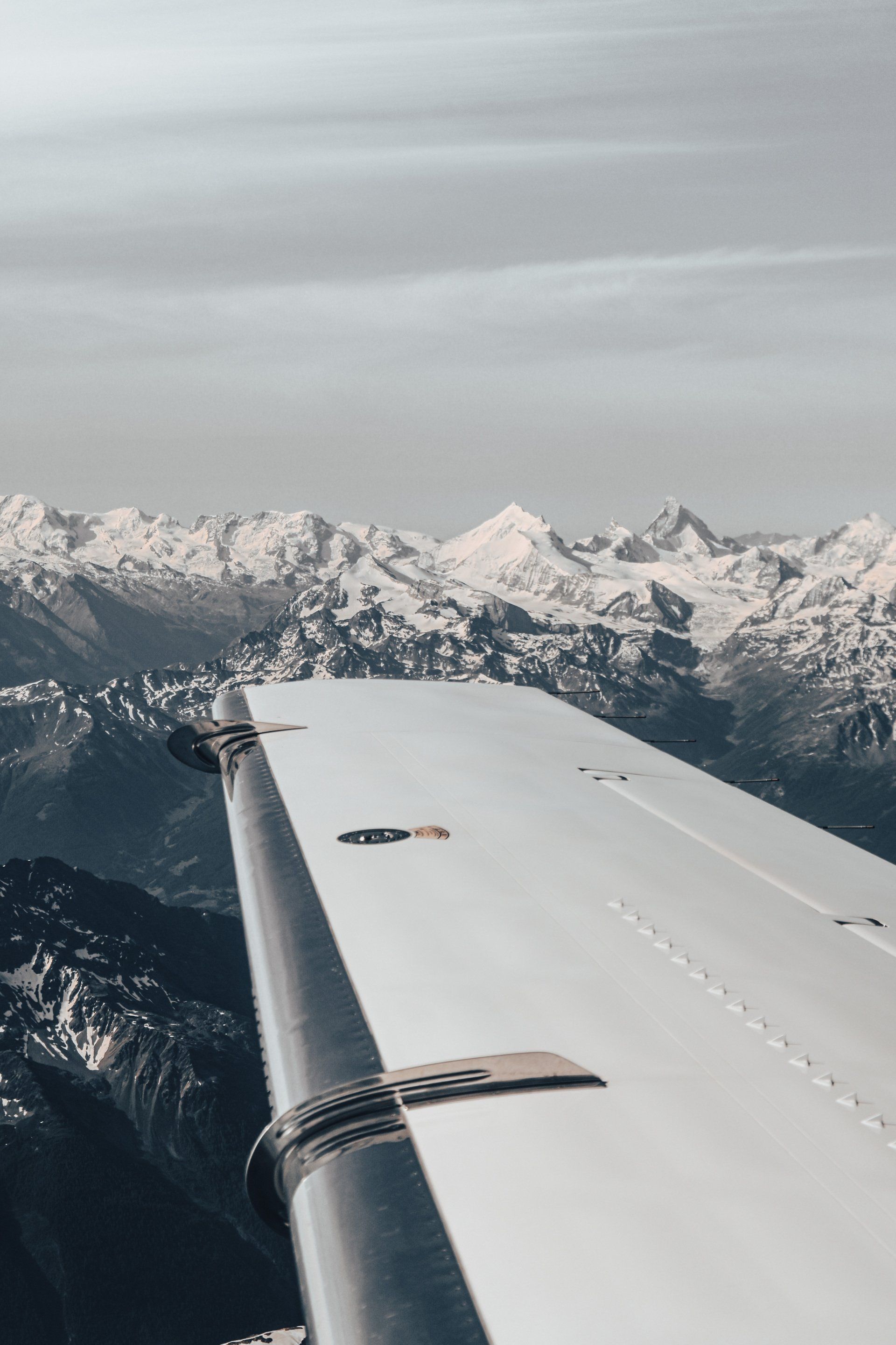 Airplane wing over snow-covered mountains under a cloudy sky