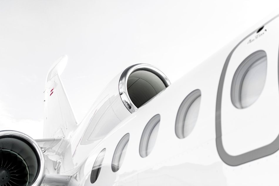 White private jet fuselage with windows and engines against a bright sky