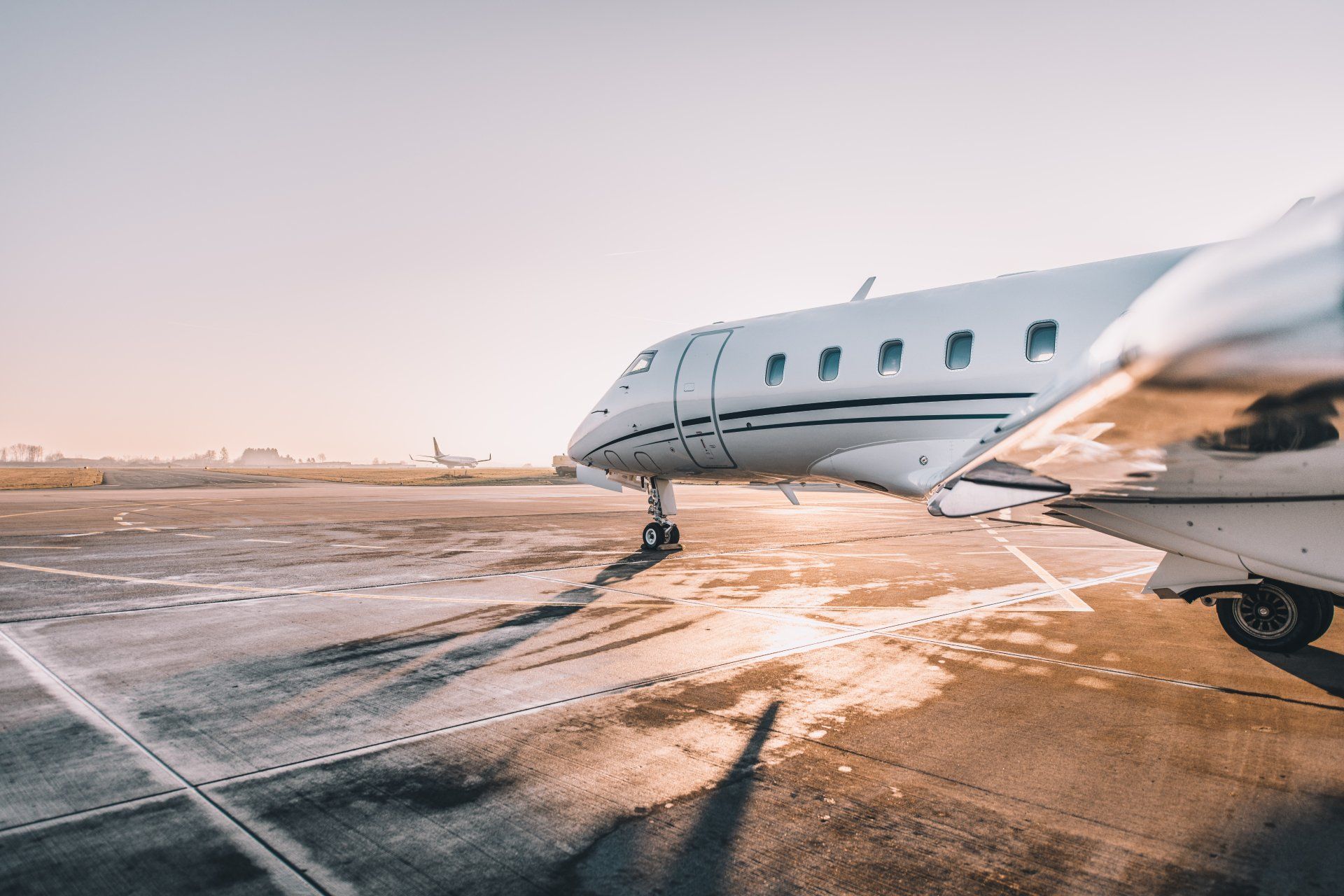 Private jet on snowy airport tarmac at sunset, with motion blur from another plane in the foreground