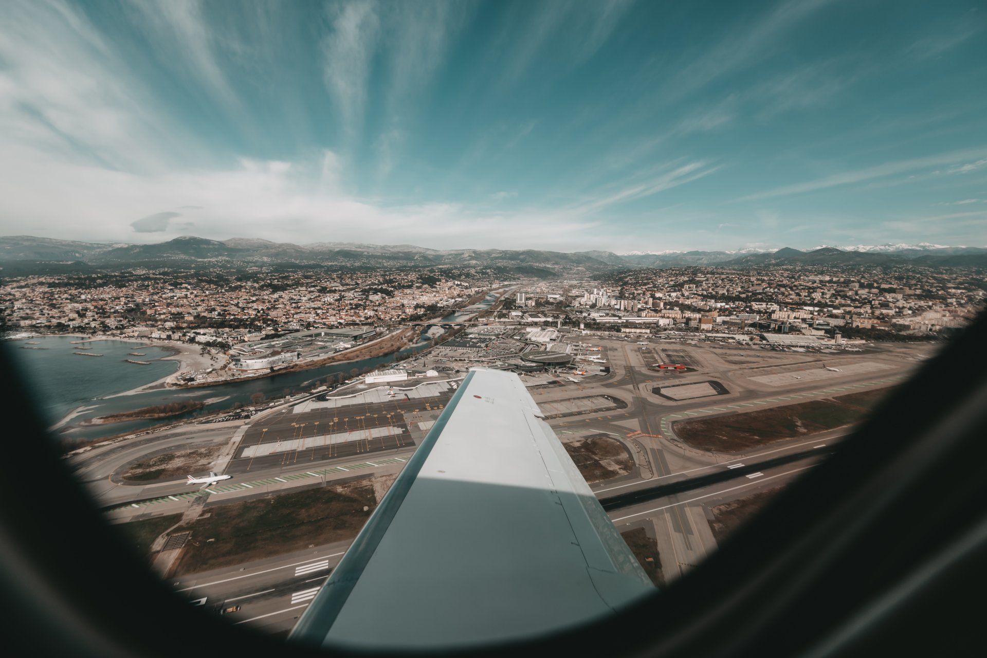 Airplane wing view over a coastal city and airport runway under a blue sky