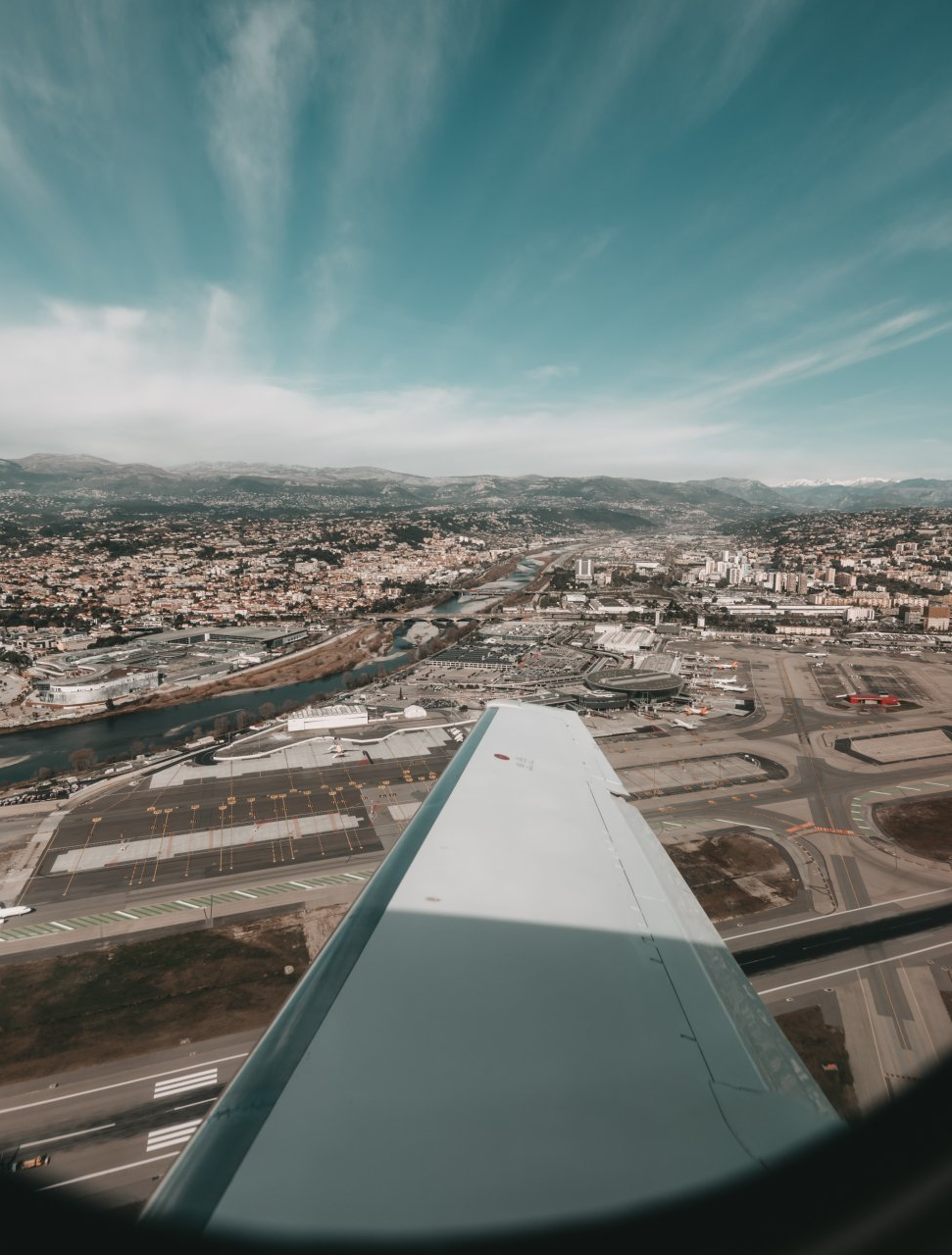 Aerial view from an airplane wing over a city and airport under a cloudy sky