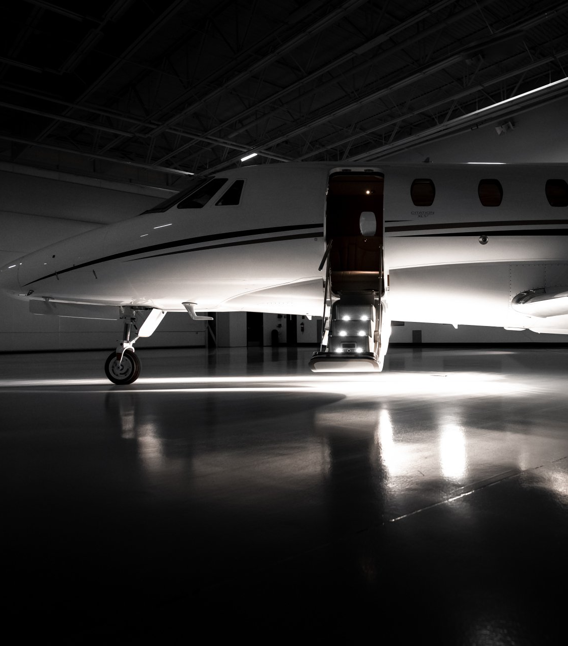 Small private jet in a dark hangar with the cabin door open and stairs lit below.