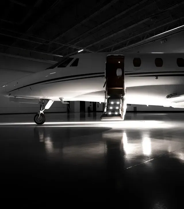 Small private jet in a dark hangar with the cabin door open and stairs lit below.