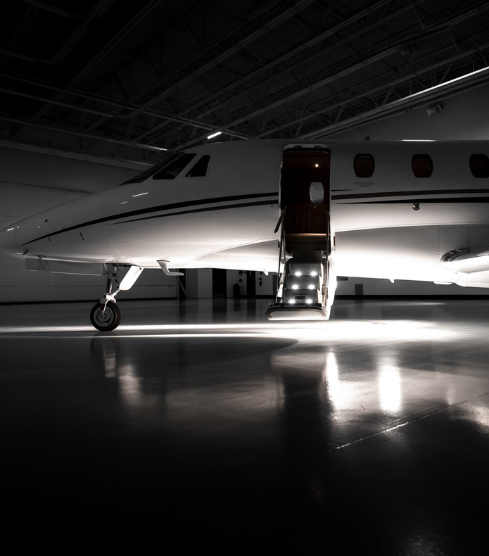 Sleek white private jet in a dim hangar with open door and lit stairs reflected on the floor
