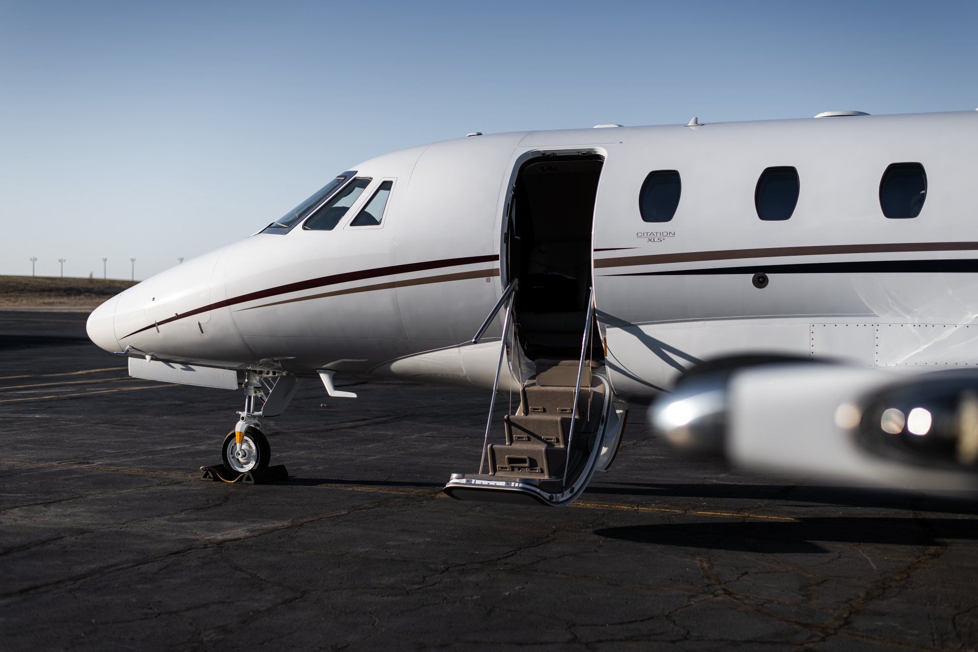 Private jet on tarmac with open door and stairs at an airport, blurred aircraft in foreground