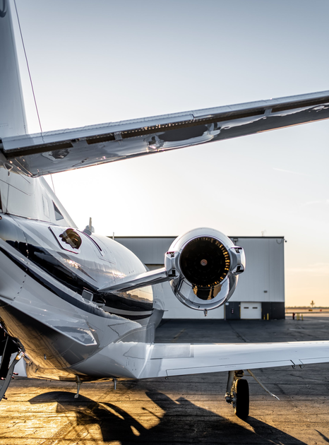 Tail section and engine of a white private jet on a tarmac at sunset