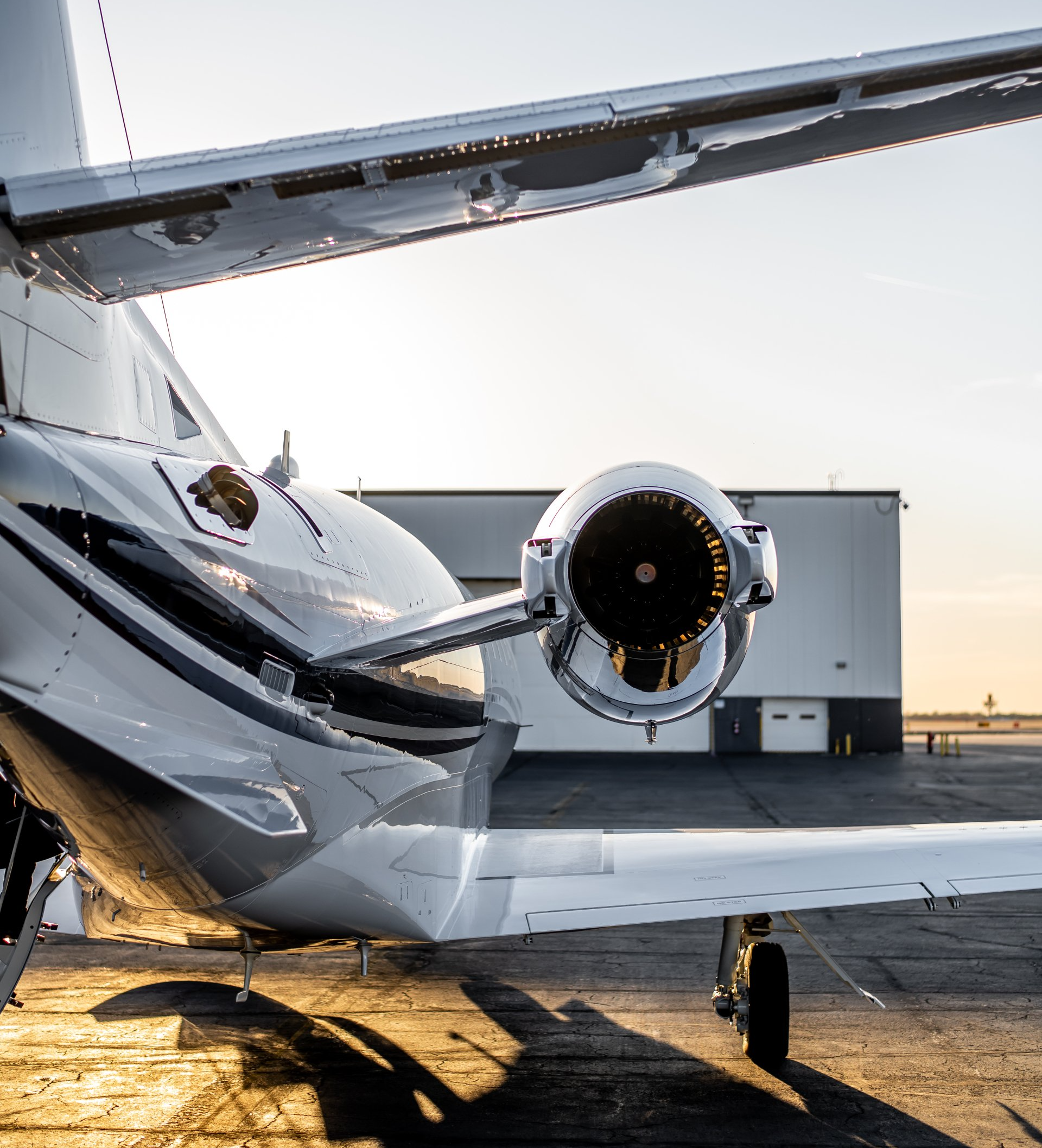 Small white airplane on a tarmac at sunset, rear engine and tail visible.