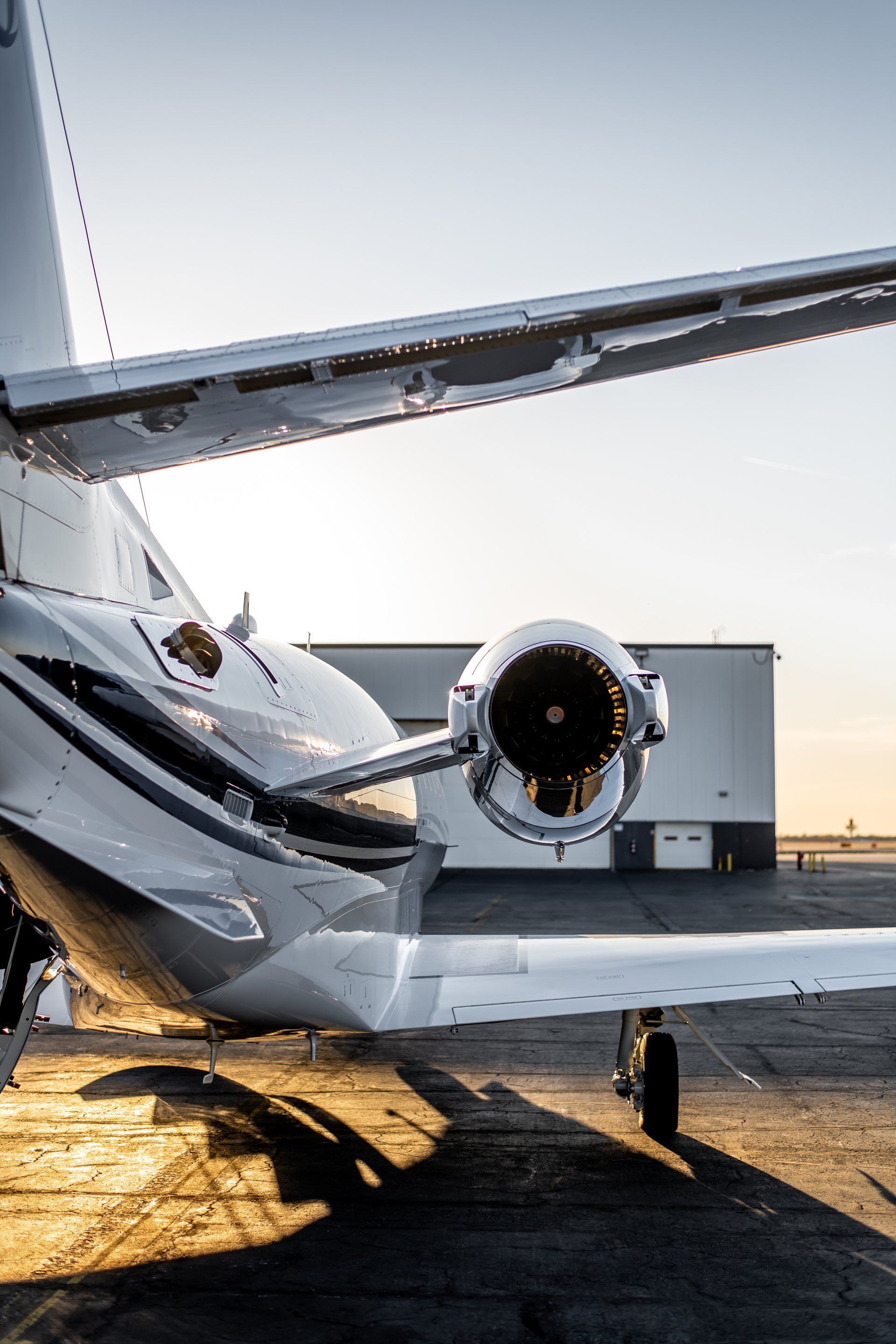 Damaged private jet on runway at sunset, with torn tail section and visible engine and wing damage