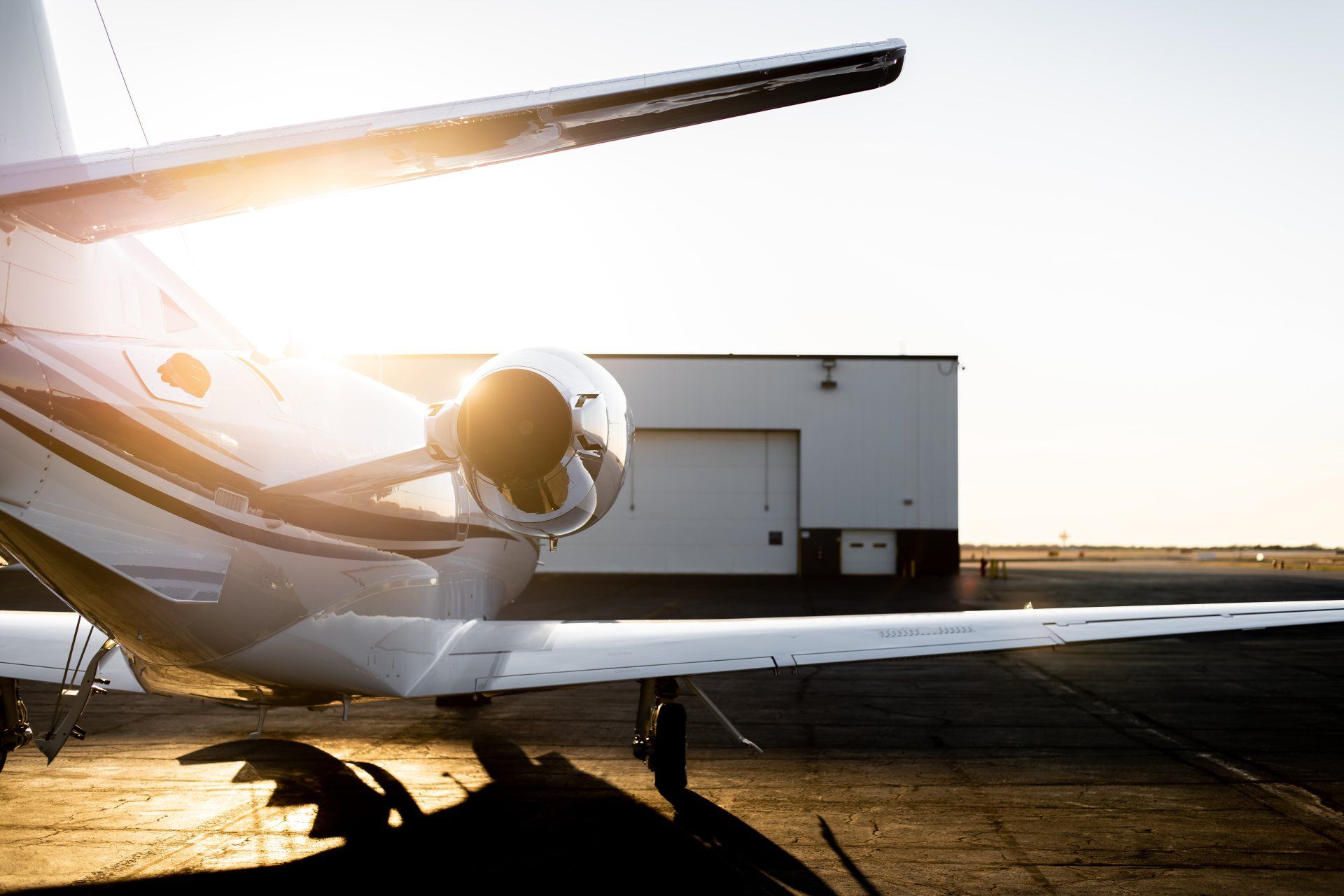 Small private jet on a runway at sunset, with bright sunlight reflecting off its fuselage.