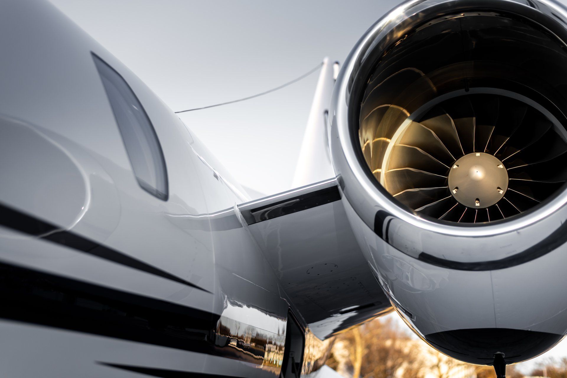 Close-up of a private jet engine on a sleek white aircraft, with flames visible below on the runway.