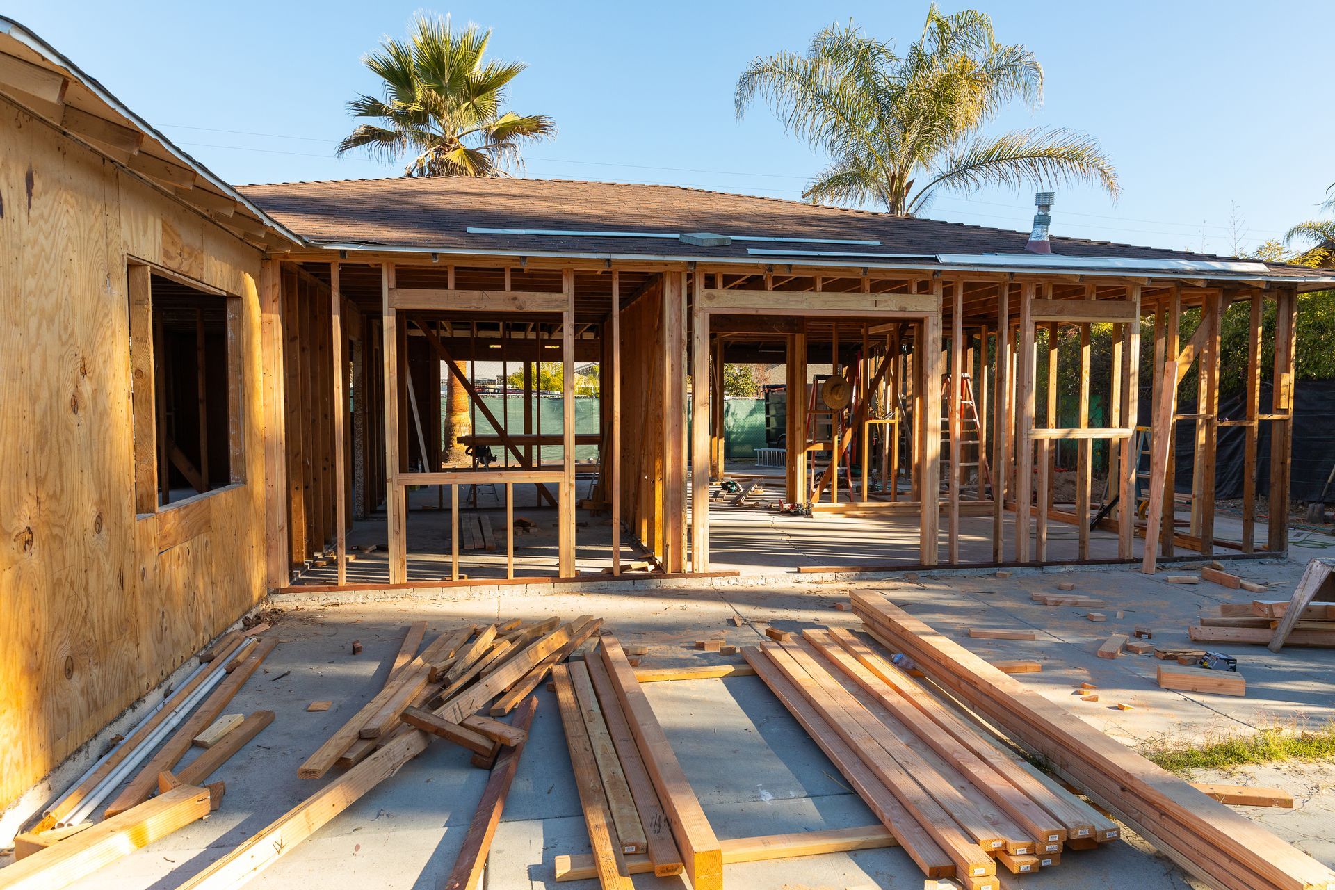 Partially built house with wooden framing and piles of lumber in a sunny yard