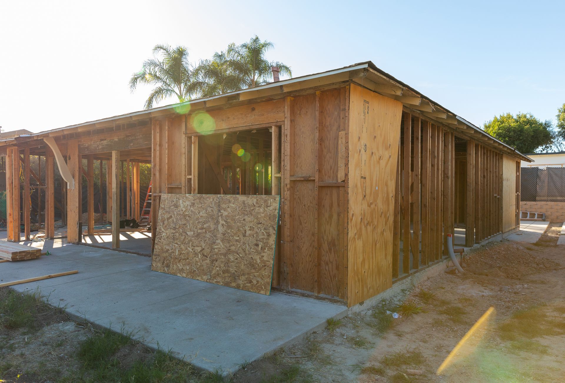 Wood-framed house under construction with plywood siding and a concrete slab foundation outdoors.