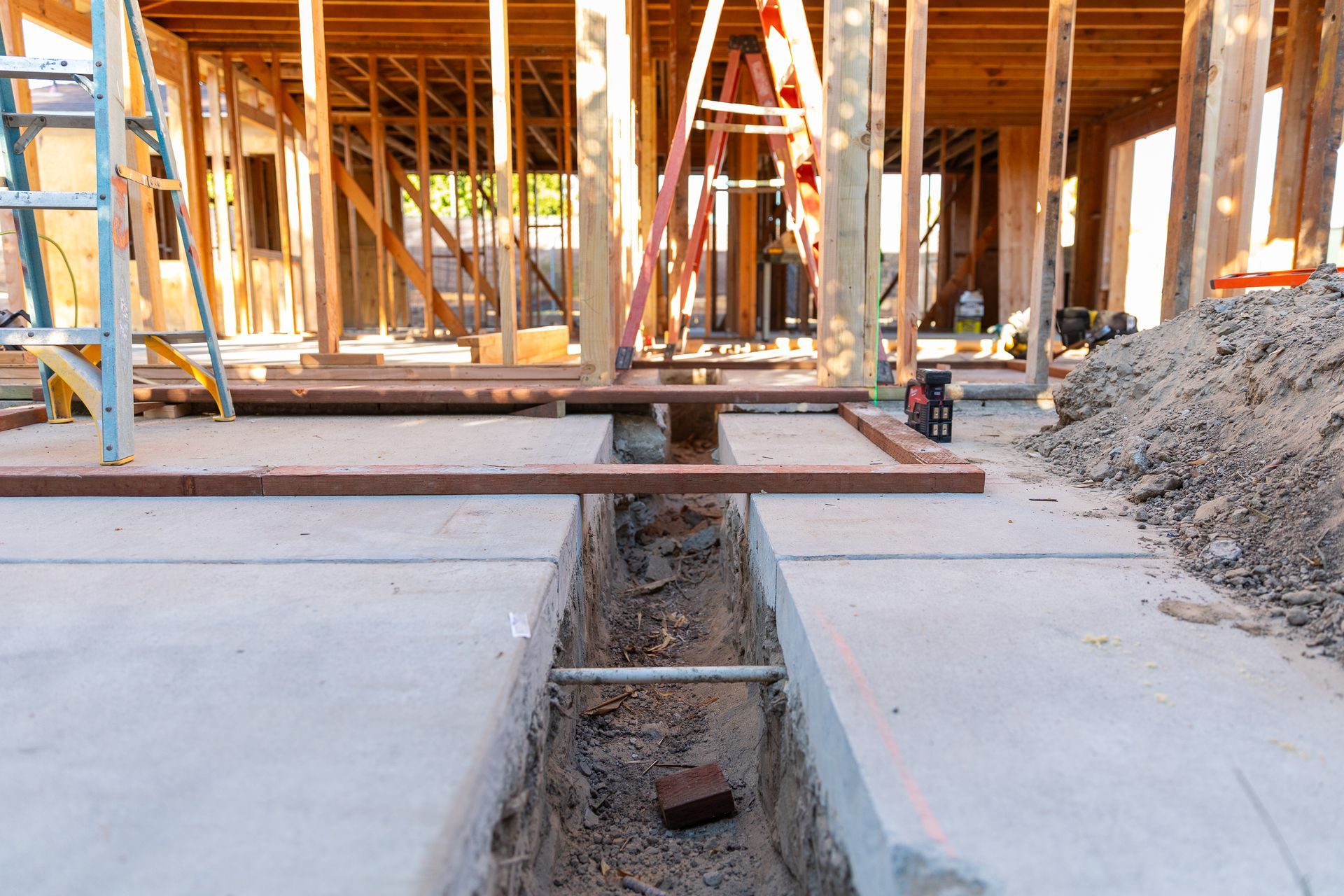 A construction site with a hole in the ground in front of a house under construction.