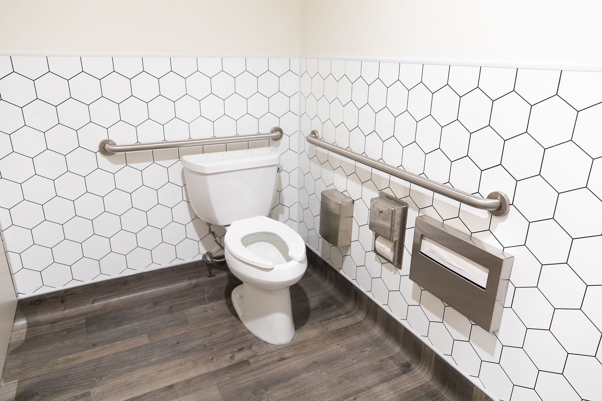 Accessible bathroom with toilet, grab bars, and wall-mounted toilet paper and waste bins