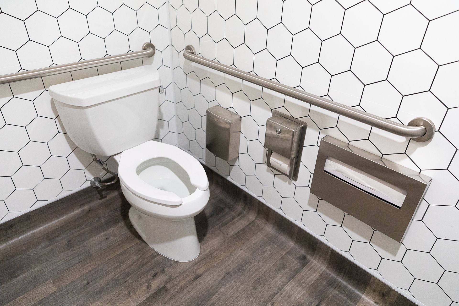 Accessible restroom with toilet, grab bars, and tissue dispensers on tiled walls