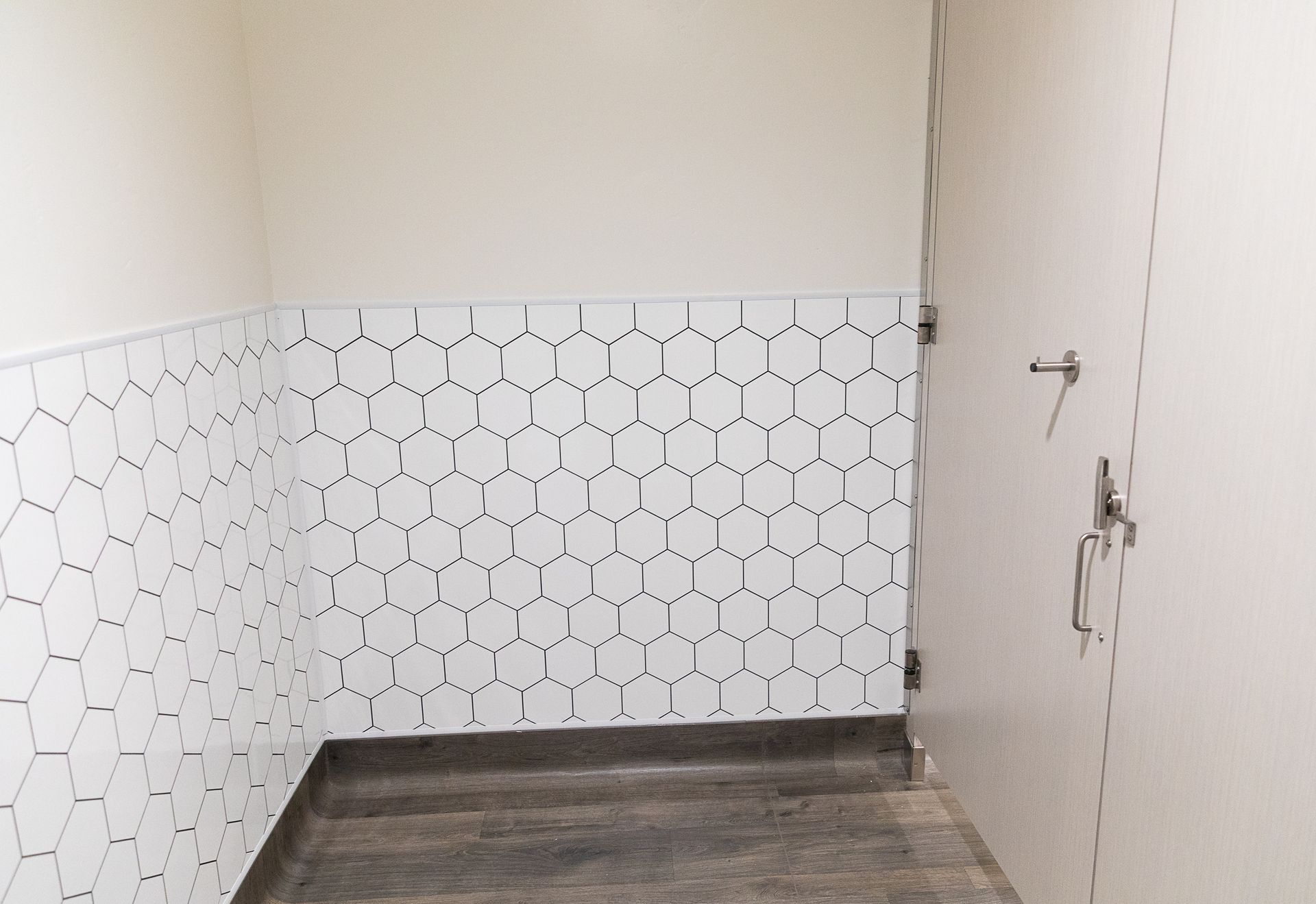 Empty room with white hex tile wainscoting, beige walls, and dark wood floor
