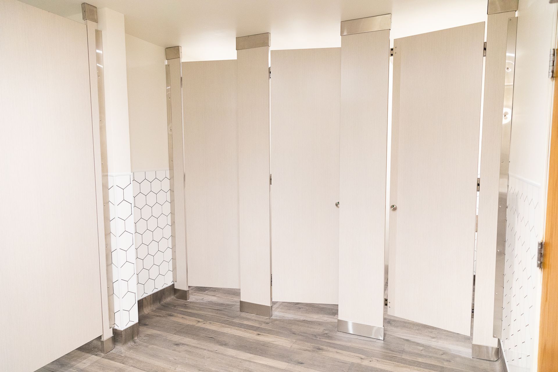 Bright restroom with several white stall doors and gray flooring