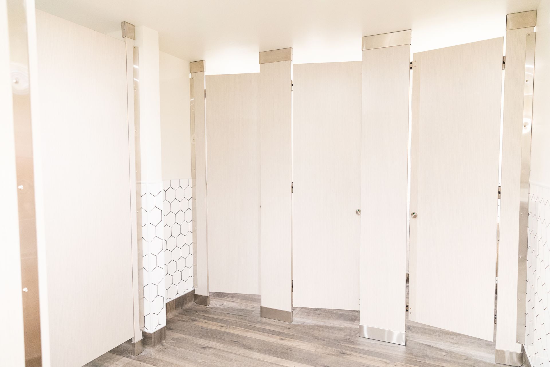 Empty restroom with white stall partitions and gray wood-look flooring